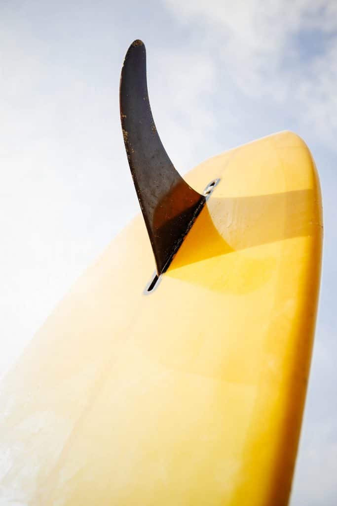 Close-up view of yellow longboard surfboard with single black fin against the sky