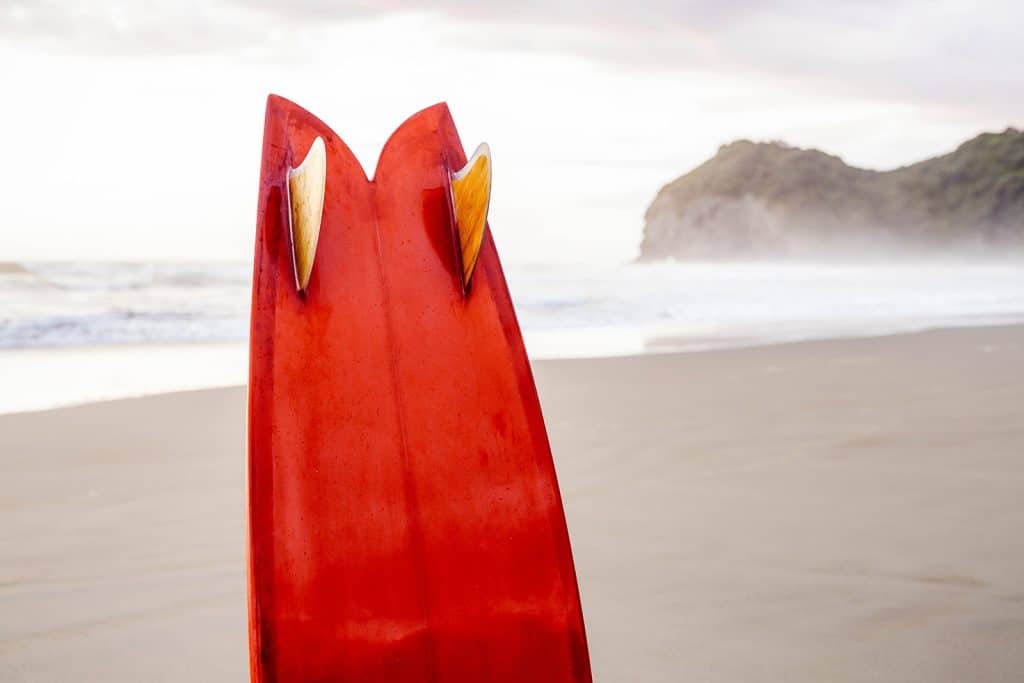 Red twin-fin fish surfboard tail shot against a foggy sandy beach