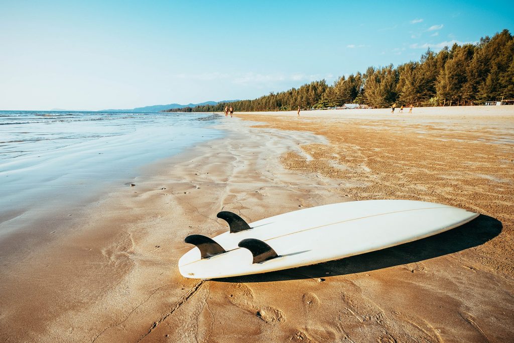 White shortboard with thruster fin setup laying on a sandy beach