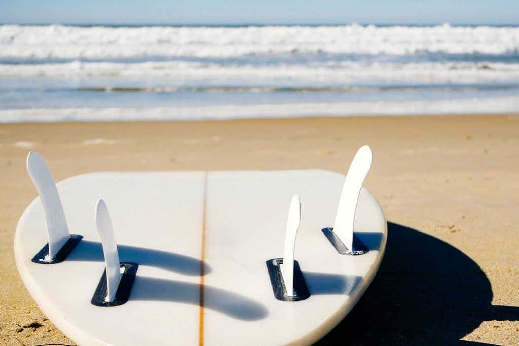 Close-up of white quad-fin shortboard placed fins up on a sandy beach