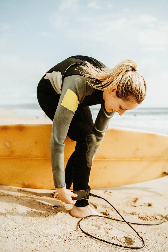 Female surfer in wetsuit attaching a surfboard leash to her ankle