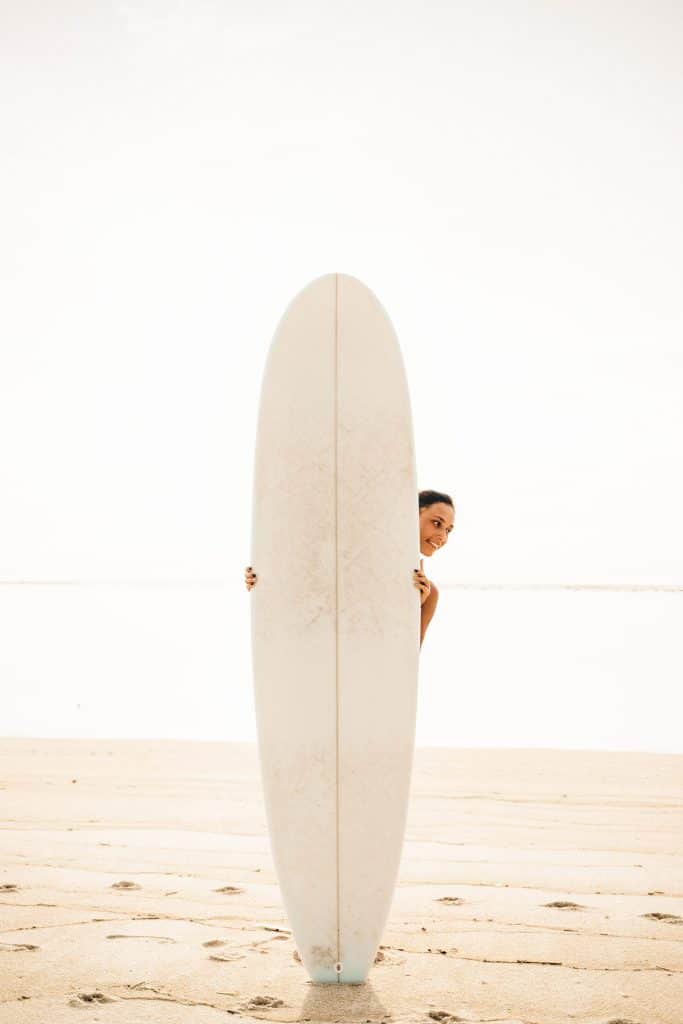 Woman standing behind a longboard surfboard on the beach