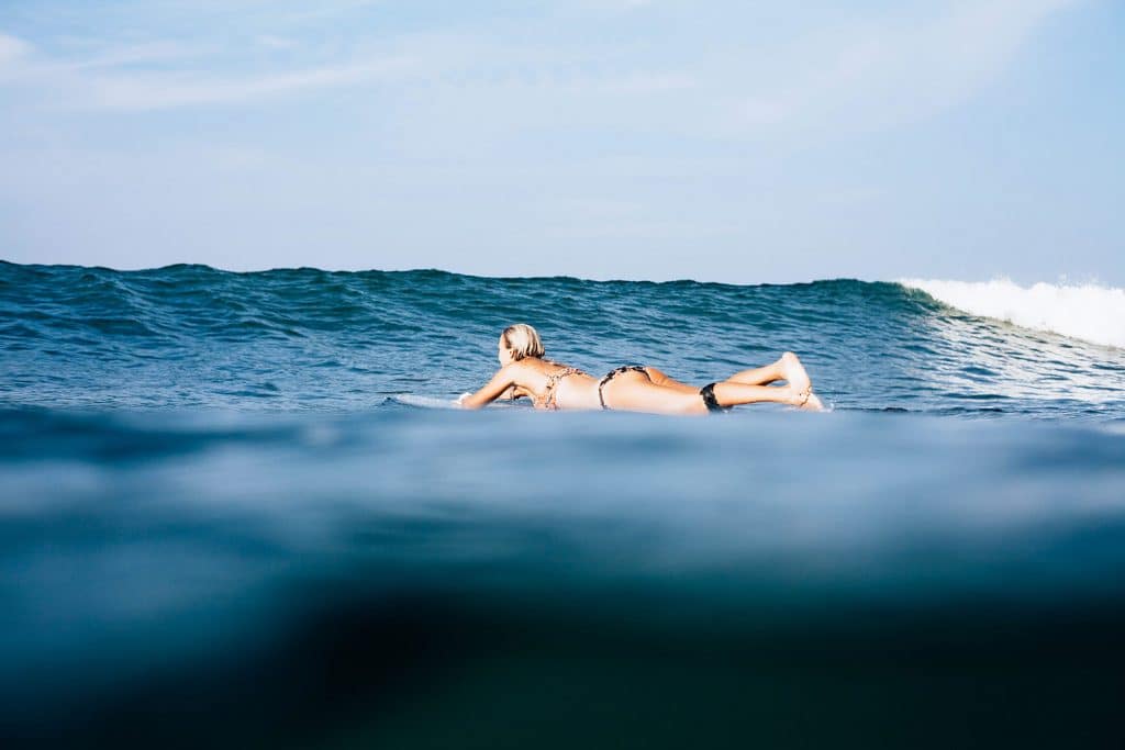 Female surfer lying on a surfboard and paddling over a small wave