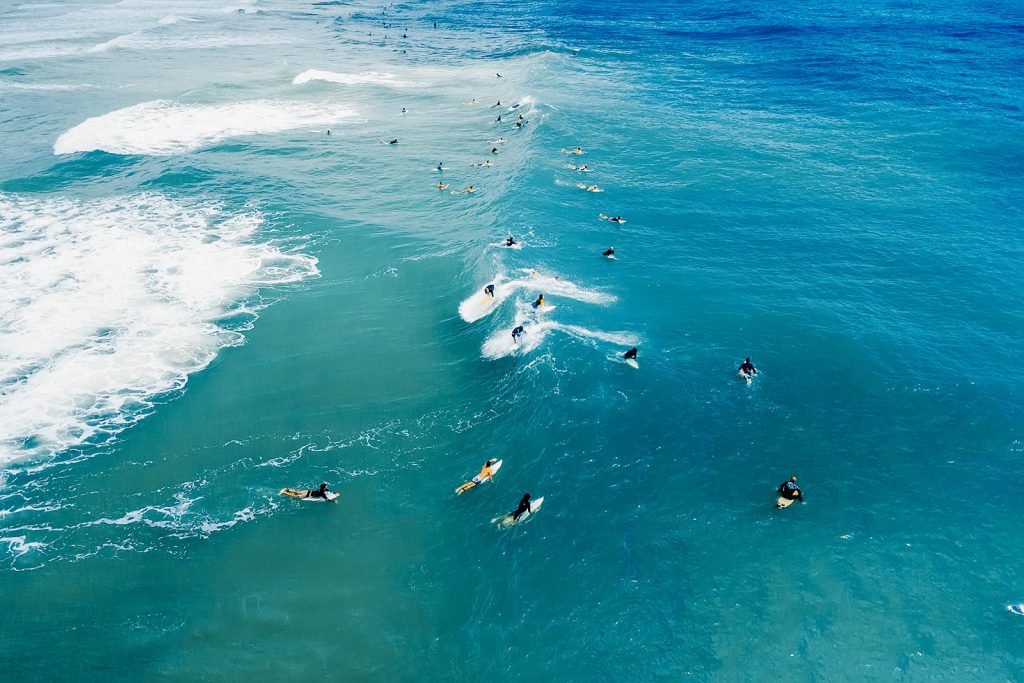Aerial shot of lots of surfers paddling over a wave