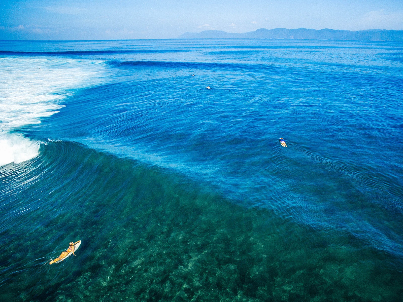 Female surfer paddling out over a reef break with clean groundswell waves